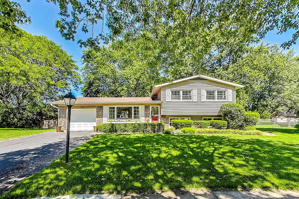 Front exterior of 318 W Hackberry, Arlington Heights — a 3-bedroom split-level home with brick and siding, a red front door, mature trees, and a generous green lawn on a quiet cul-de-sac.
