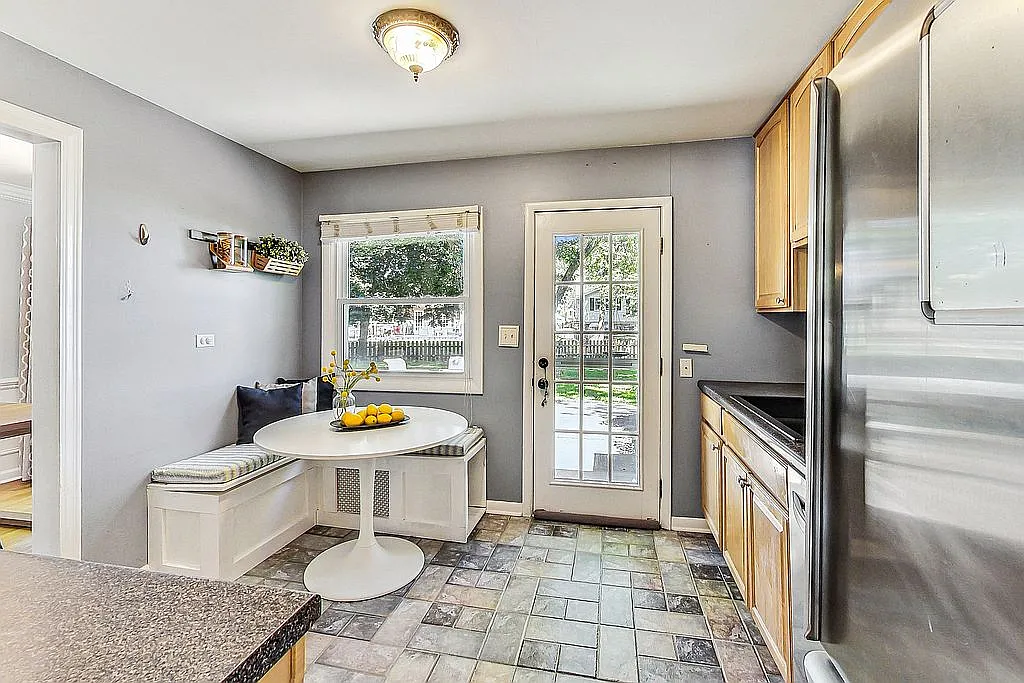 Kitchen breakfast area with a round white tulip table, a built-in corner bench seat with striped cushion, gray walls, and a glass-paned door leading out to the patio.