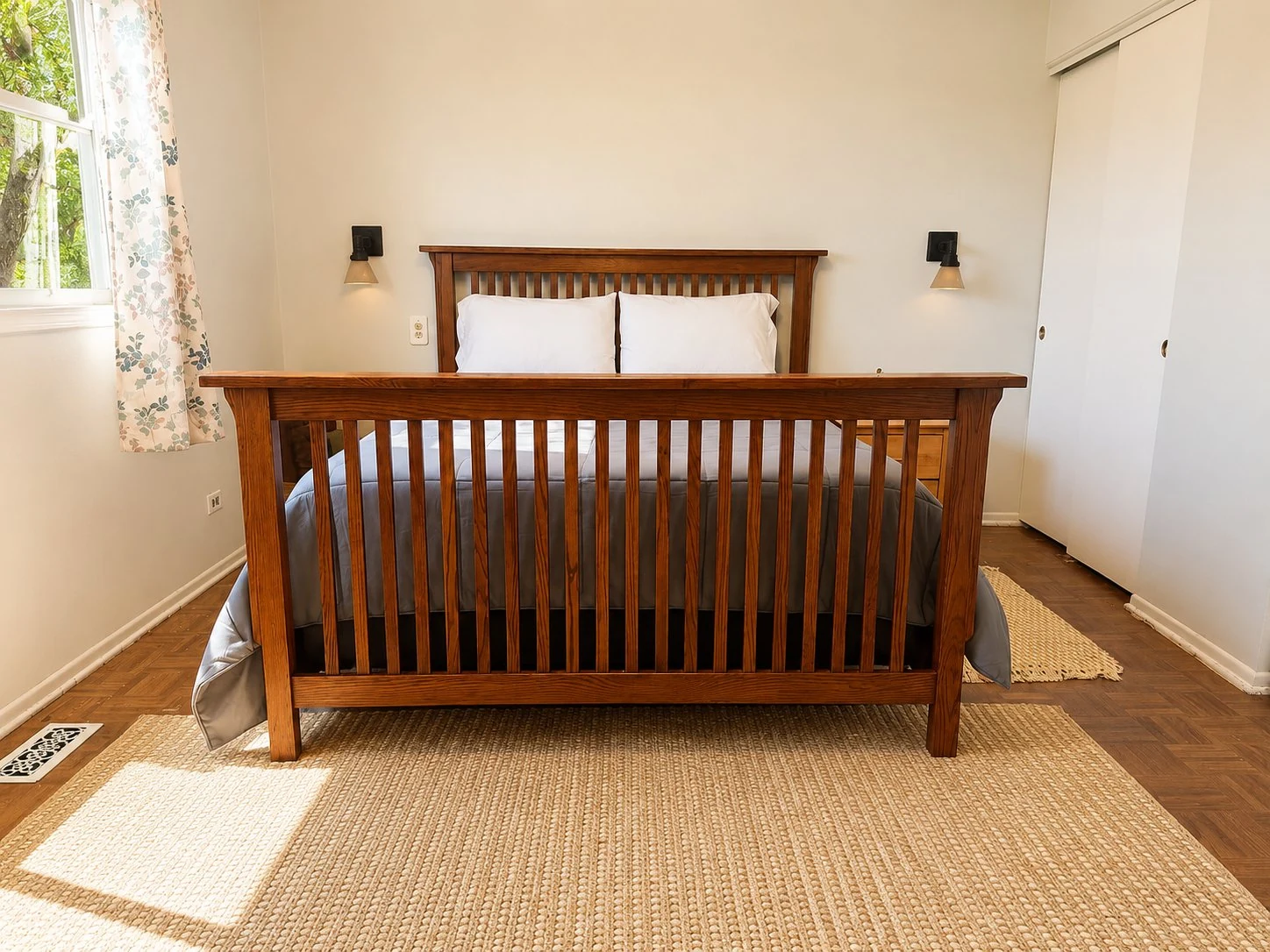 Primary bedroom with a Mission-style oak bed frame and headboard, queen mattress with gray bedding, hardwood parquet floors, woven area rug, wall sconces, and a sliding-door closet.