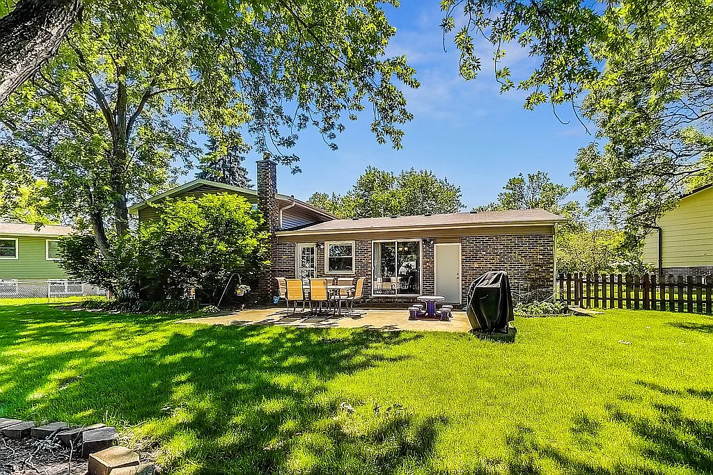 Rear view of the home showing the brick exterior, patio, and a spacious fully fenced backyard with a level green lawn and mature shade trees.
