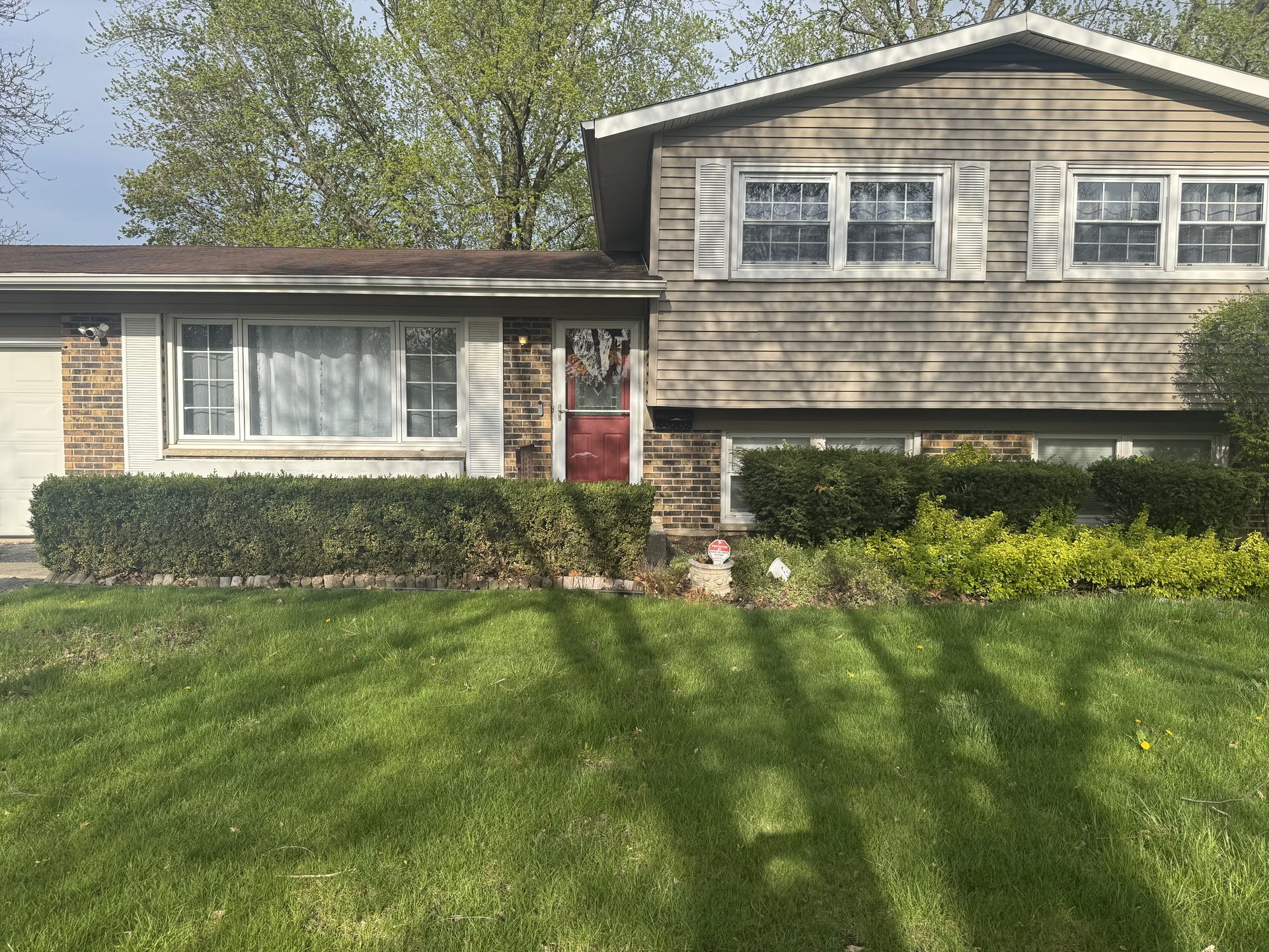 Front exterior of 318 W Hackberry, Arlington Heights — a 3-bedroom split-level home with brick and siding, a red front door, mature trees, and a generous green lawn on a quiet cul-de-sac.