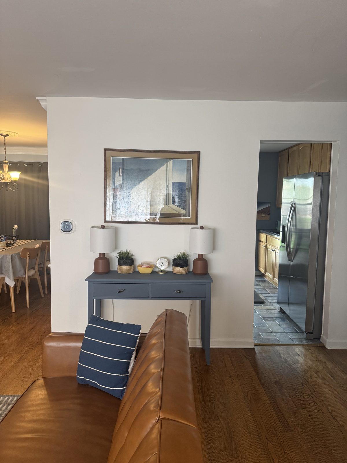 View from the living room across the open floor plan toward the dining room and kitchen, showing the home's natural flow with a navy console table and stainless-steel refrigerator visible beyond.