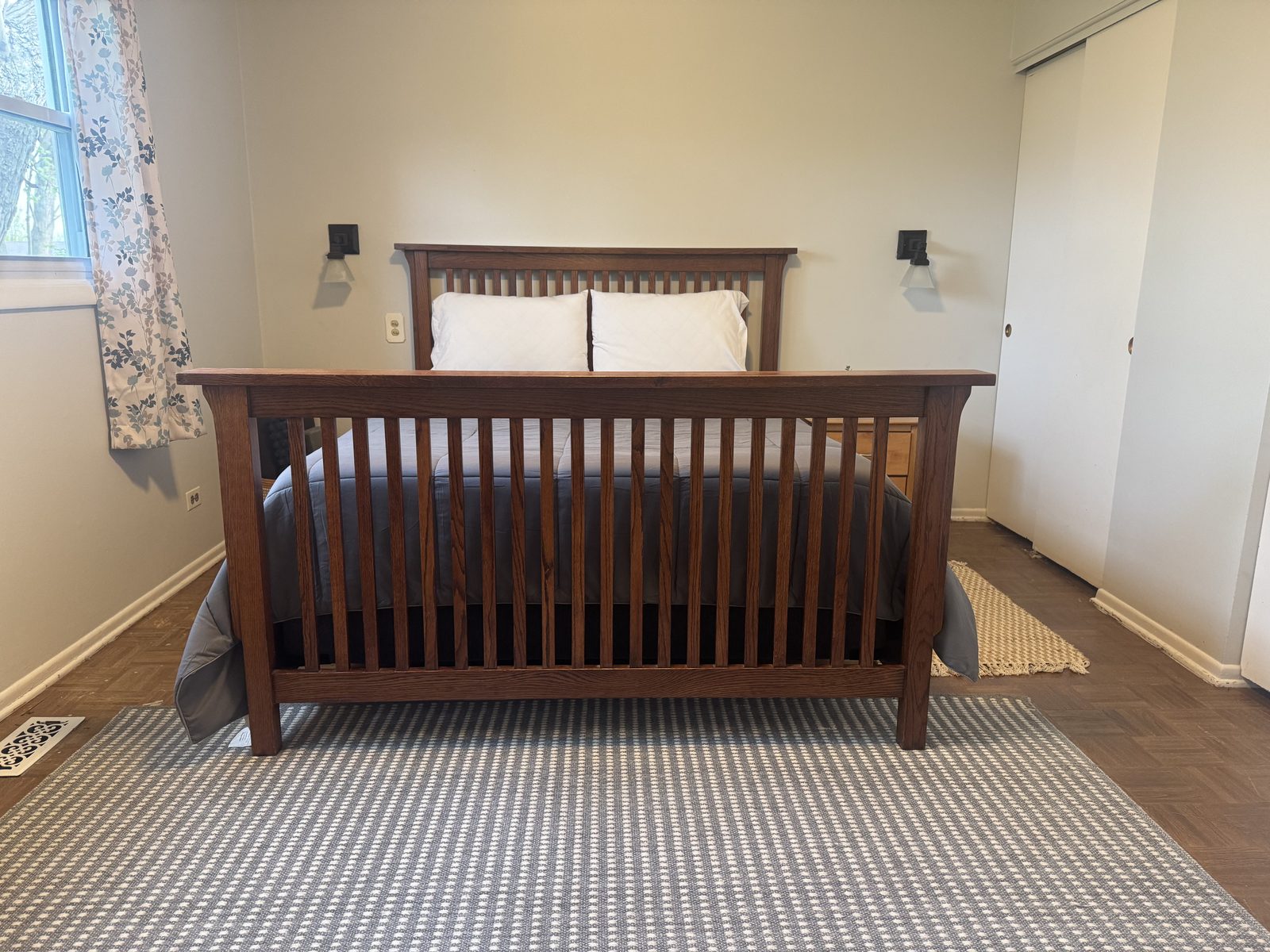 Upper-level primary bedroom at 318 W Hackberry with a Mission-style oak bed frame, queen mattress with white linens, original hardwood parquet floors, sconce lighting, and sliding closet doors.